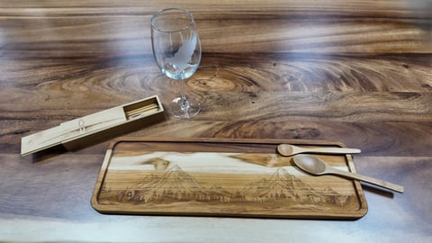 Engraved wooden serving tray with a mountain scene, two wooden spoons, a wooden box and an etched wine glass